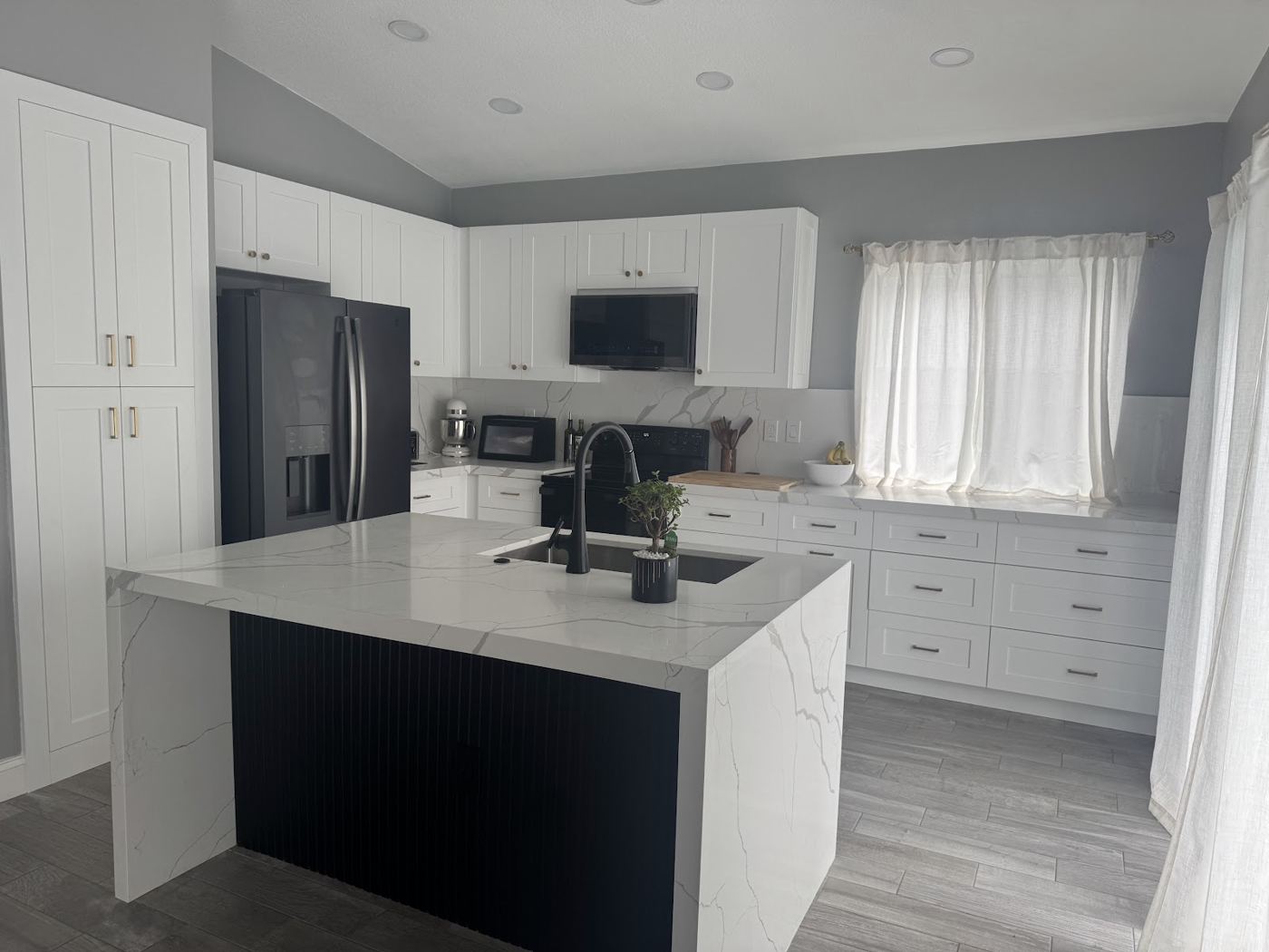 Cocina terminada con isla negra y encimera blanca en cascada